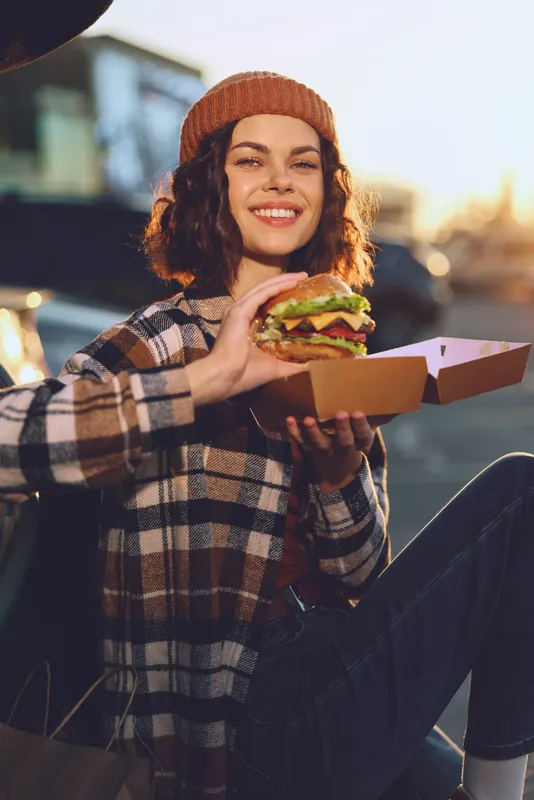 Woman burger takeaway smile candid lifestyle outdoors urban scene with authenticity, golden hour glow and mindful living, emotional storytelling in a relaxed street food portrait moment