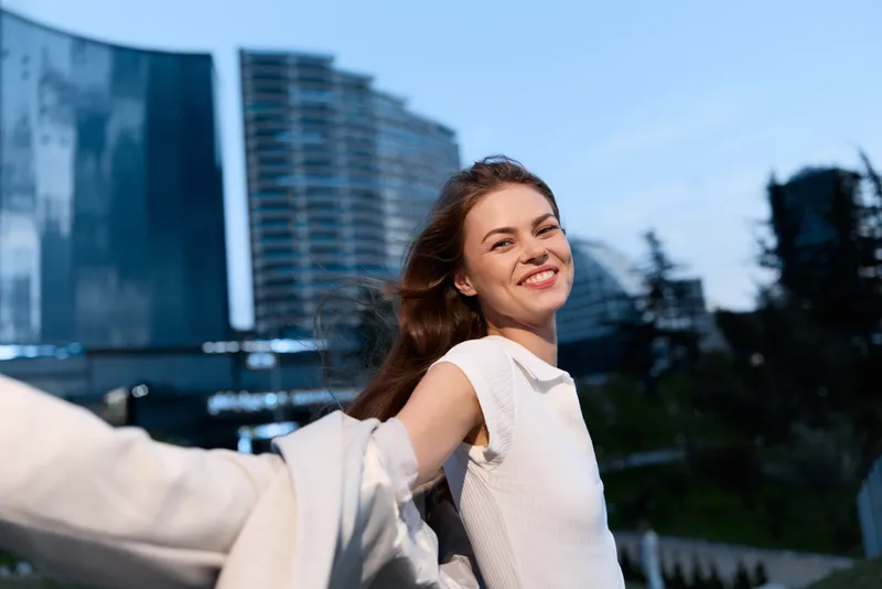 Confident businesswoman smiling outdoors with modern architecture in the background, showcasing empowerment and professionalism in a stylish urban setting.