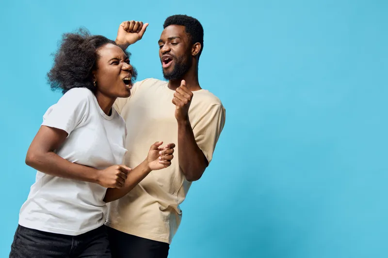 A joyful young African couple dancing together against a vibrant blue background, expressing happiness and excitement in casual clothing
