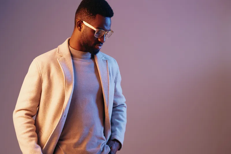 Stylish African American man in casual outfit, wearing glasses, showcasing self confidence against a smooth gradient background in pastel colors