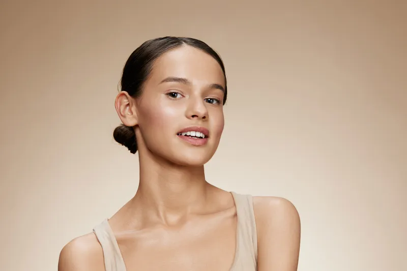 Smiling young female model with natural makeup and neutral background showcasing beauty and skincare concepts in a soft, warm color palette