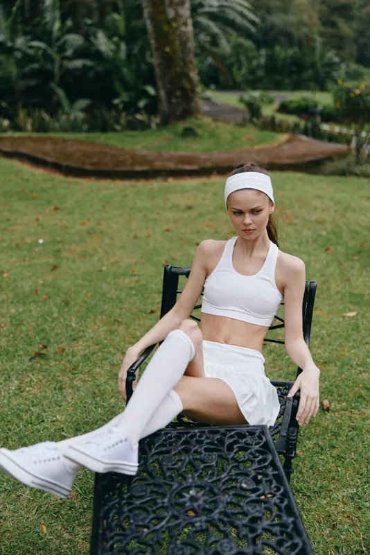 A fit model in a stylish white sports outfit poses gracefully in a lush green garden, showcasing a confident expression and athletic elegance, perfect for fitness themes
