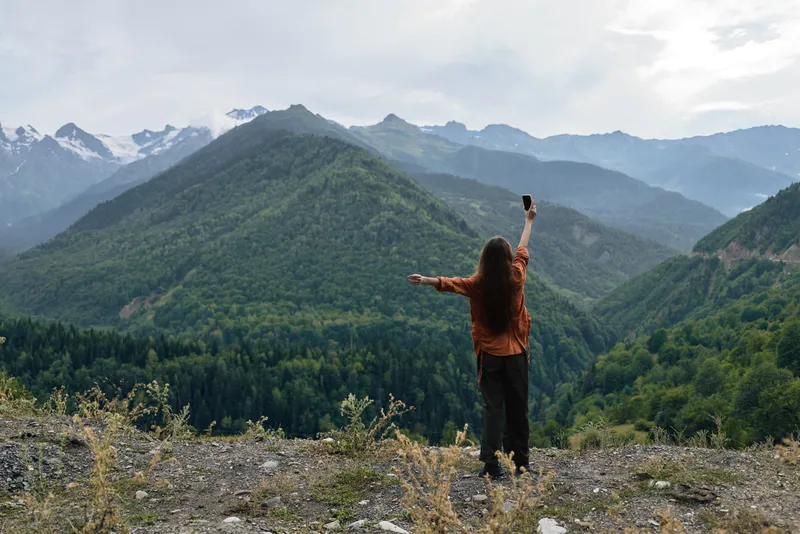 Adventure in vast nature as a lone traveler stands on rocky ground with arms raised, embracing mountains and expansive landscape under clear sky