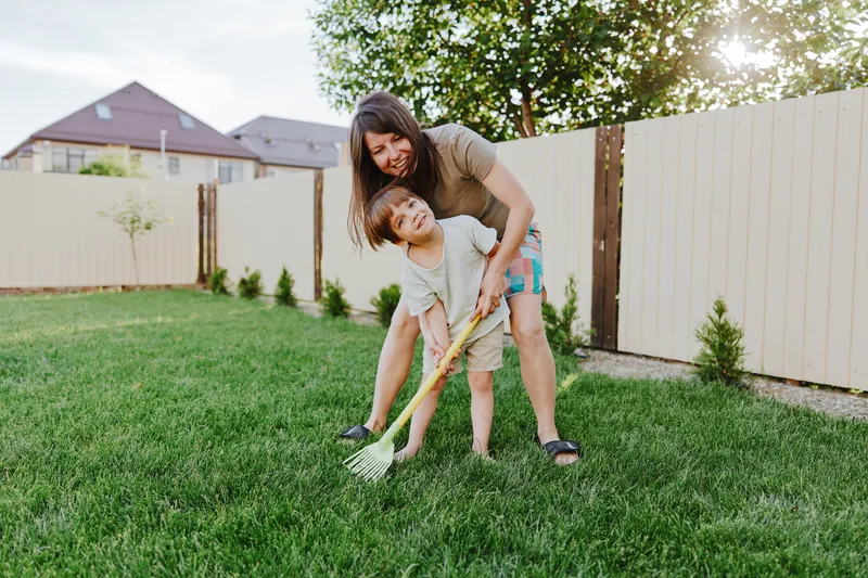 Joyful woman gardening with her son, enjoying quality time outdoors while caring for a green lawn in a sunny backyard setting.