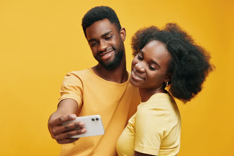 Joyful couple taking a selfie against a vibrant yellow background, showcasing their happiness and love in casual summer attire