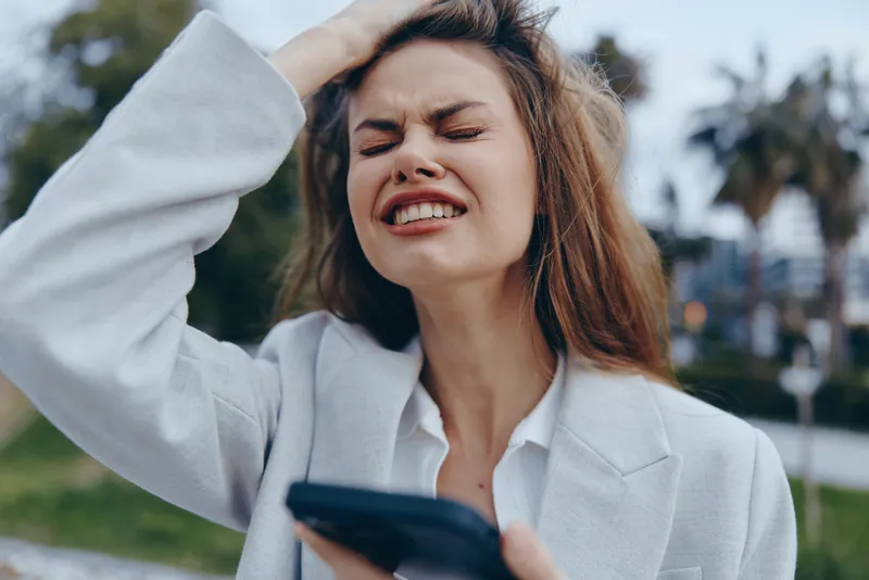 Frustrated businesswoman struggling with work-related stress outdoors, showcasing emotions in a professional setting amidst a modern backdrop.