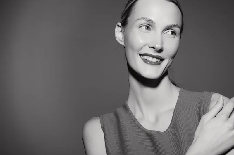 Smiling caucasian woman with light skin and slicked back hair looks aside wearing sleeveless top in studio. Concept of natural beauty and elegance.