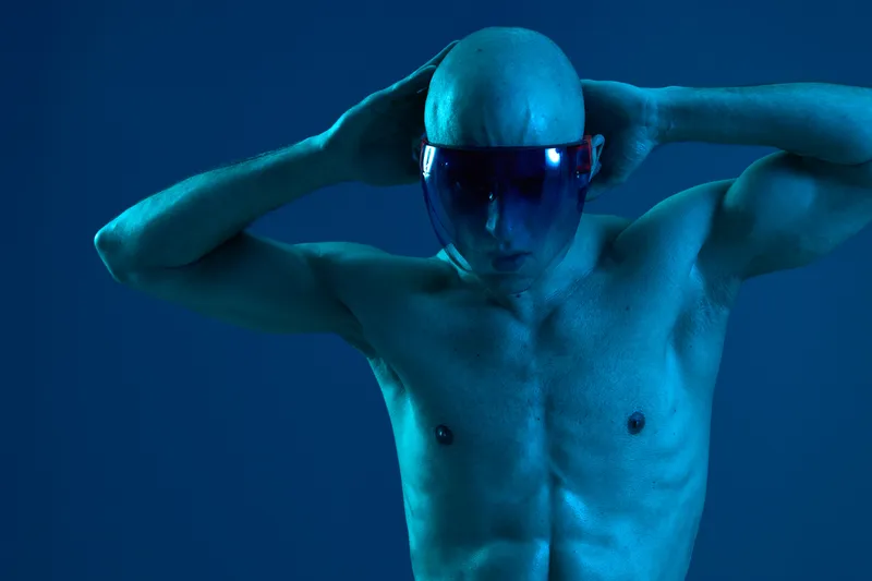 Athletic man with a futuristic look, wearing a visor and striking a confident pose against a blue background. This black and white image emphasizes strength and style.