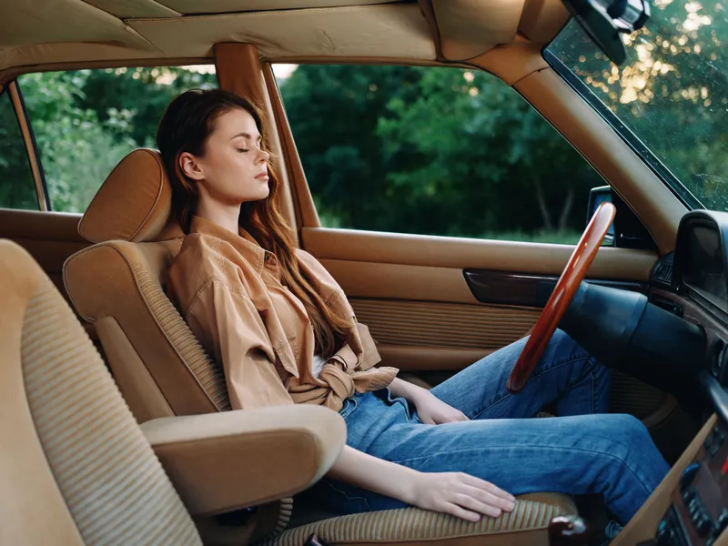 Young woman in a vintage car, enjoying a moment of tranquility outdoors, showcasing a relaxed expression and casual attire in beige and denim.