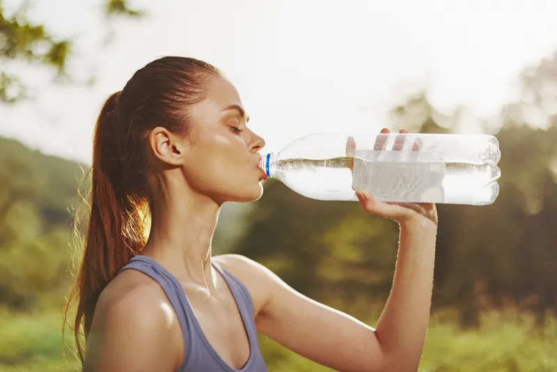 Young woman drinking water outdoors, promoting healthy hydration and an active lifestyle in a natural setting