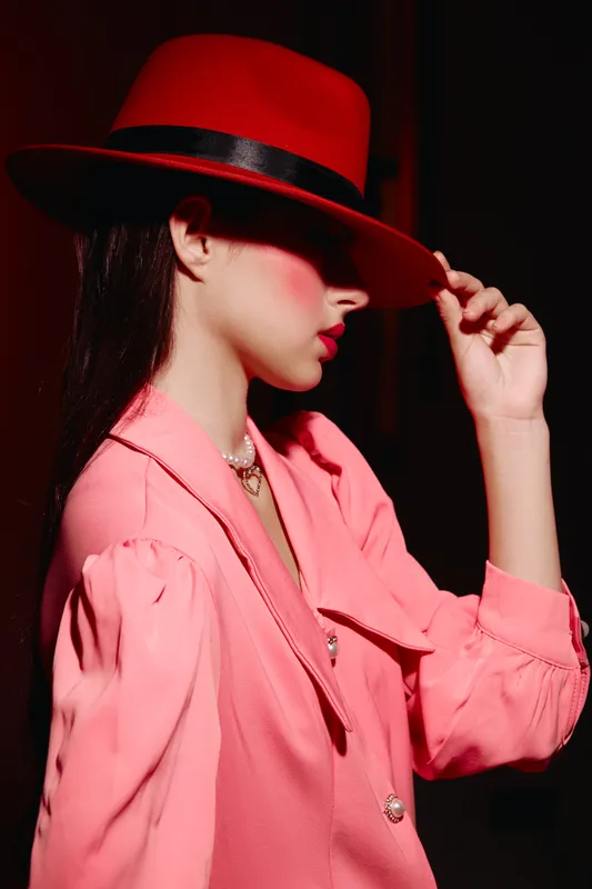 Young woman in a red hat and pink blouse poses with side profile in studio lighting. Concept for fashion, beauty, glamour, and elegant style creative portraits.