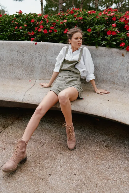 Young woman in casual summer outfit sits on a stone bench surrounded by vibrant flowers, reflecting a carefree attitude and connection with nature