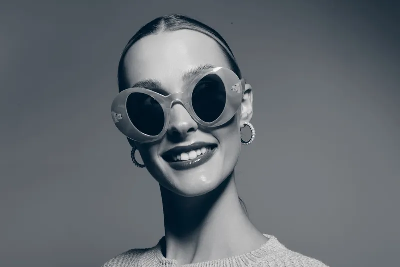 Smiling white woman with fair skin wearing round sunglasses and hoop earrings in studio portrait. Concept of fashion and happiness.