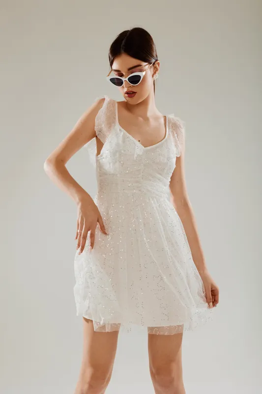 Young woman in a white lace dress and stylish sunglasses poses confidently against a neutral background. Concept of beauty, fashion, elegance, and modern style.