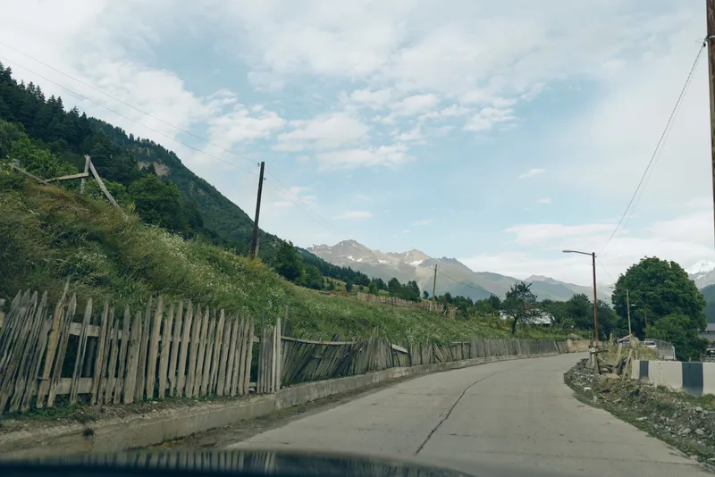 mountain road fence village countryside sky landscape nature rural asphalt road with wooden fence green hills and distant peaks
