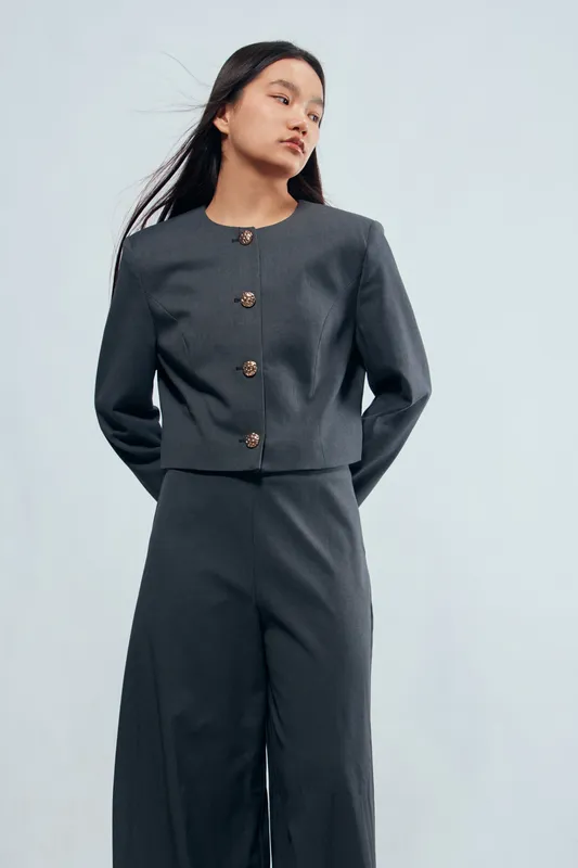 Woman in gray pantsuit with buttons poses looking to side on light background. Fashion, style and confidence for casual or office outfit with minimal design and long hair.