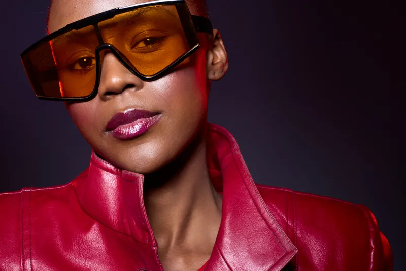 Close-up of confident black woman with dark skin wearing oversized orange sunglasses and red leather jacket. Studio portrait with dramatic lighting and fashion concept for style and attitude.
