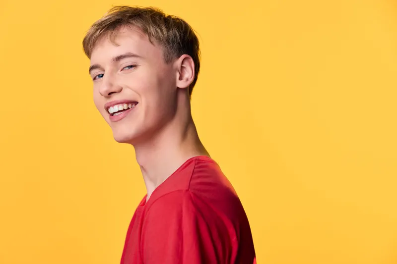 Smiling man in a red shirt against a vibrant yellow backdrop captures a cheerful mood, contemporary style, and versatile appeal for lifestyle, fashion and advertising imagery