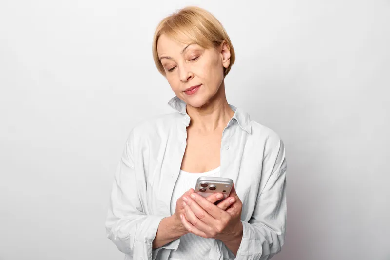 Woman holding smartphone shows stress and anxiety, tired gaze downward, woman in white blouse, loneliness and healthcare mental health concept, communication theme, quietly