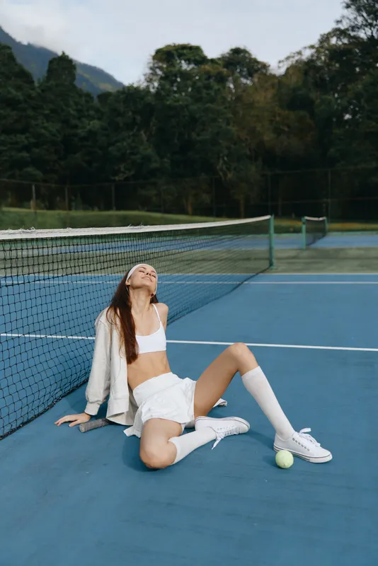 Young female athlete in white sportswear posing on a tennis court, showcasing confidence and joy while enjoying the sport