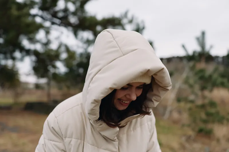 Hooded jacket, woman, outdoor, smiling, nature, cold weather portrait showing cozy style in a field setting with warm tones and candid mood for lifestyle stock