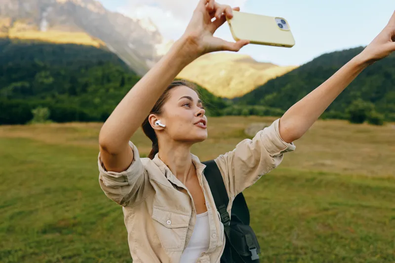 Bright outdoor moment with a woman lifestyle outdoors selfie in a mountain nature travel smiling casual portrait, sunlit backdrop and lush scenery