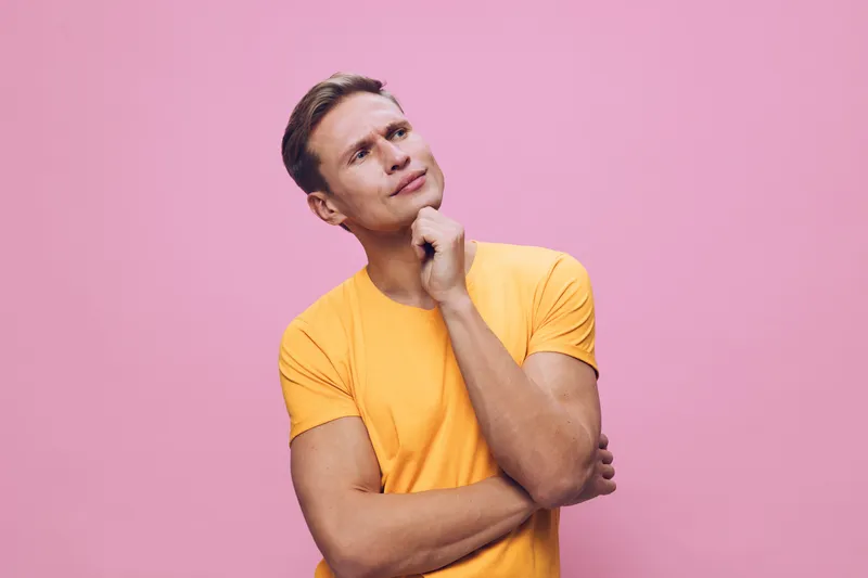 thoughtful man wearing yellow t-shirt looking up pink background mental health and gadgets concept portrait