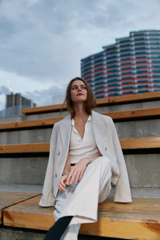 Confident woman in business attire sitting on steps against a city backdrop, showcasing modern elegance, professional demeanor, and urban sophistication.