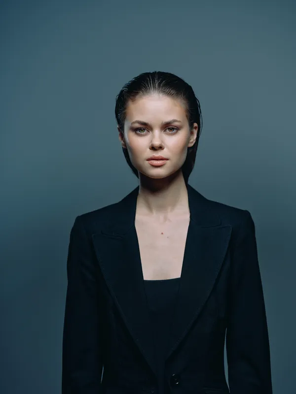 serious woman wearing black blazer with slicked-back hair against dark background