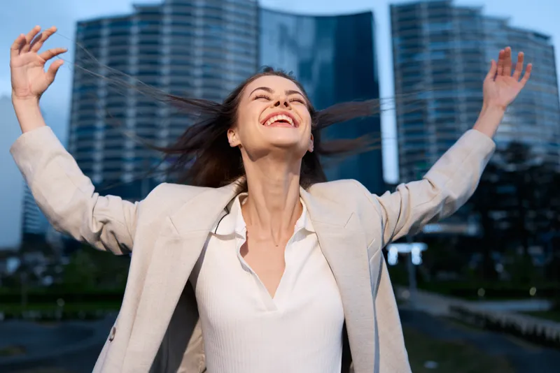 Confident businesswoman joyfully celebrating success in an urban environment with modern architecture, expressing empowerment and professionalism.