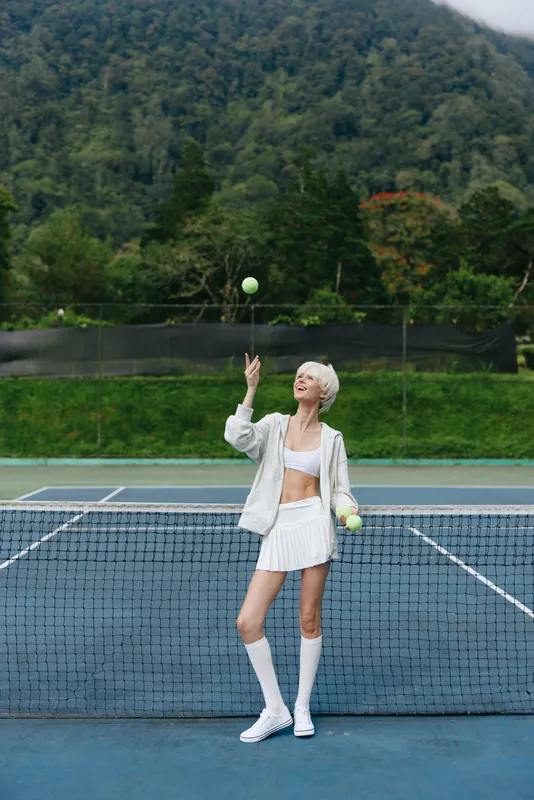 Young woman with short blonde hair in sportswear playing tennis outdoors, showcasing a joyful emotion and vibrant green background