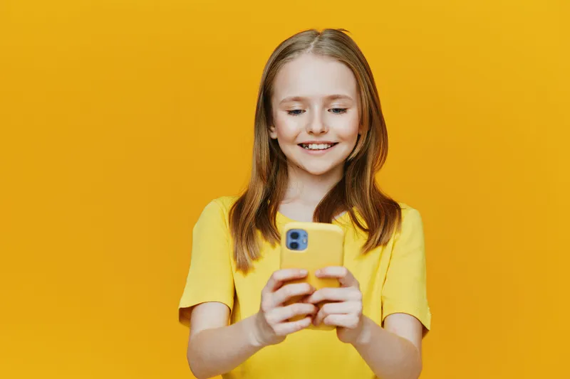 Happy girl with smartphone wearing yellow shirt against yellow background, smiling and enjoying technology, perfect for vibrant lifestyle and social media themes