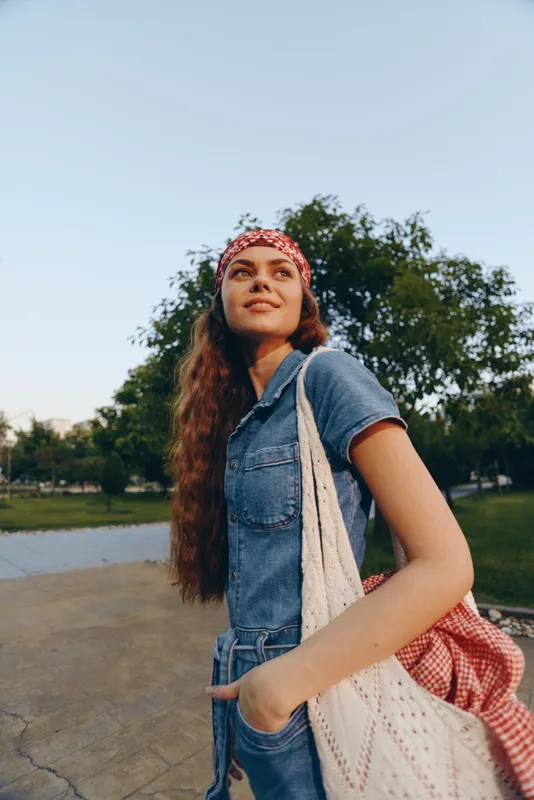 Lifestyle woman in modern boho-western denim street style smiling confidently outdoors with film color effect during sunny day near green trees and river.