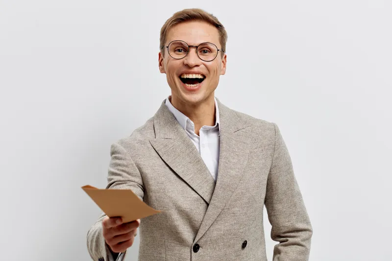 Smiling man in beige blazer holding a mobile phone, looking cheerful and confident, studio portrait with plain light background, professional, business, happy expression, technology, lifestyle.