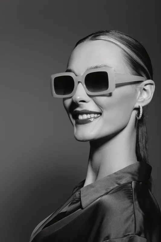 Smiling caucasian woman with light skin wearing sunglasses and earrings in a studio portrait. Stylish fashion concept with confident expression.
