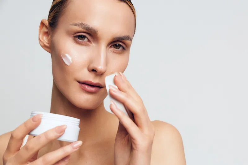 Woman skincare beauty closeup, apply face cream with cotton pad during routine, hydration and skin care concept, young calm female portrait in bright studio white background, soft glow