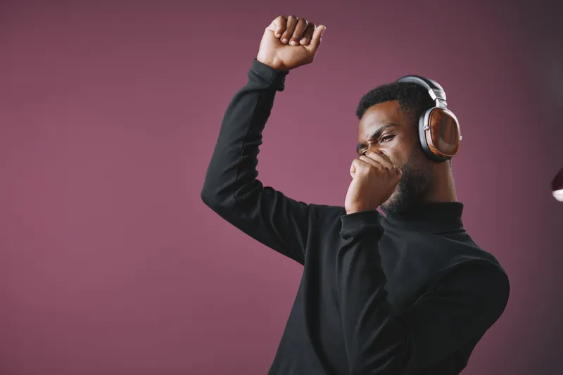 Young Black man enjoying music with headphones, expressing joy and movement against a stylish purple background Perfect for themes of music and emotion