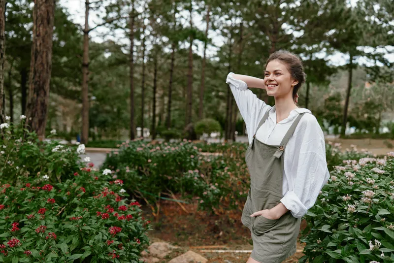 Young woman in casual outfit smiling in a blooming garden, surrounded by vibrant flowers and greenery, embodying joy and nature in springtime