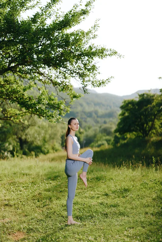 Young woman practicing yoga in a serene green landscape, showcasing flexibility and peace with natural mountain background and soft lighting