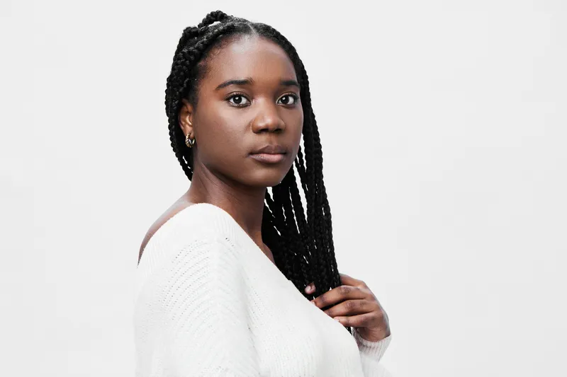 Elegant young Black woman with long braided hair wearing a cozy white sweater, soft expression, and neutral background, perfect for fashion and lifestyle content