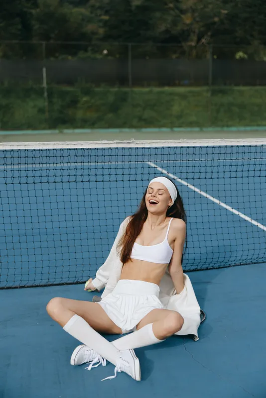 Happy young woman in sporty outfit laughing on tennis court, showcasing athletic wear, joyfulness, and vibrant colors in a seasonal outdoor setting