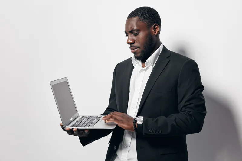 Black man in business suit using laptop computer for work or communication on white background. African ethnicity, dark skin, professional and focused with technology.