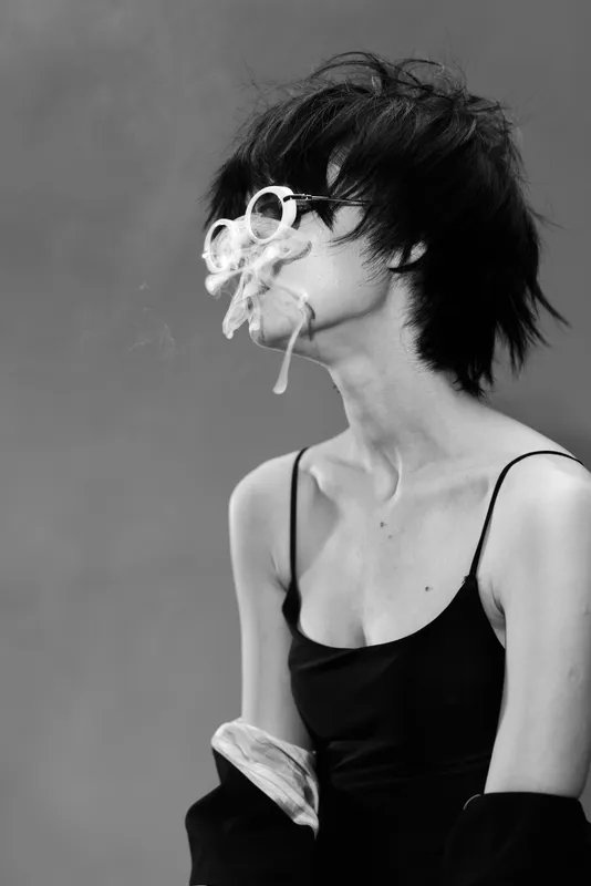 Black and white portrait of a young woman with short dark hair in a black dress with artistic flowers on her face.