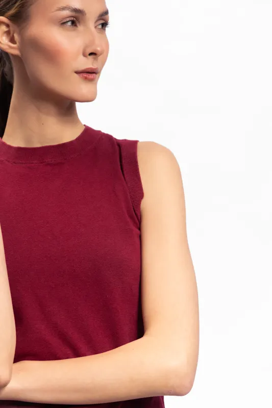 Young woman with smooth skin wears sleeveless burgundy top, looking sideways with thoughtful expression on white background. Concept for fashion, beauty, and portrait photography.