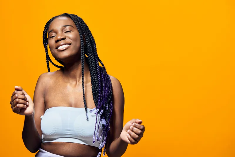 Happy young woman with braided hair against a vibrant yellow background, showcasing joy and confidence while dressed in a stylish crop top