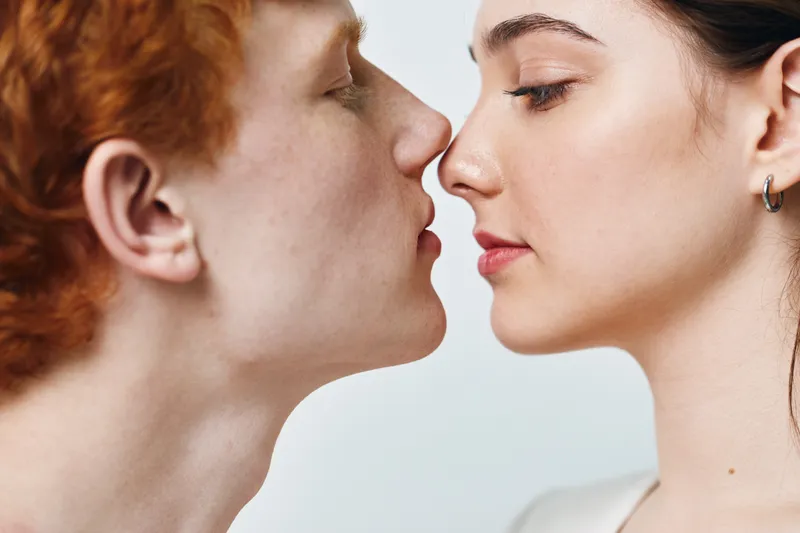 Couple, young man and woman face close together with eyes closed and tender expressions for love, romance and intimacy in studio portrait with white background.