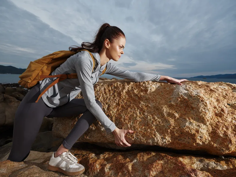 Athletic woman climbing a rock at the beach, showcasing determination and strength in sportswear, perfect for fitness and adventure themes