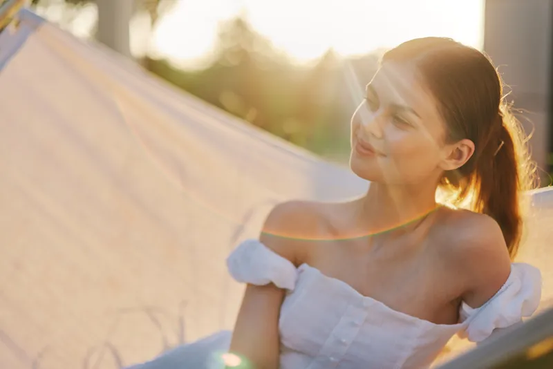 A young woman enjoying a serene moment in a hammock during sunset, wearing a light summer dress and exuding confidence and tranquility