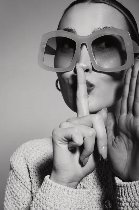 Young caucasian woman with fair skin wearing oversized glasses makes shushing gesture. Concept of silence and secrecy.