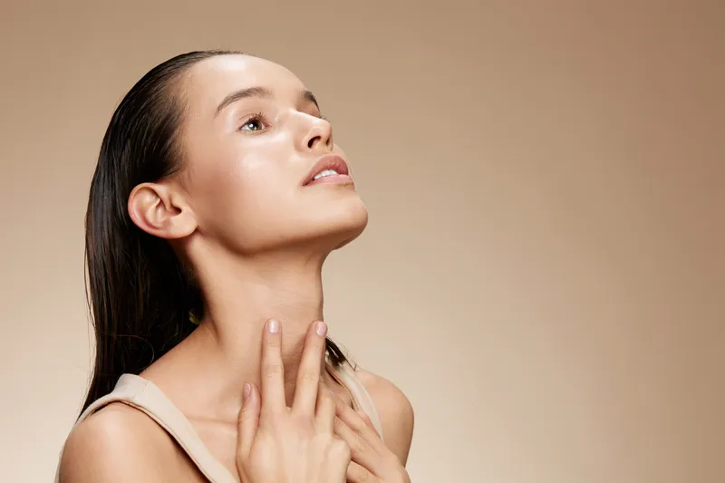 Young woman with glowing skin looking upward against a neutral background, expressing serenity and self care, perfect for wellness and beauty concepts